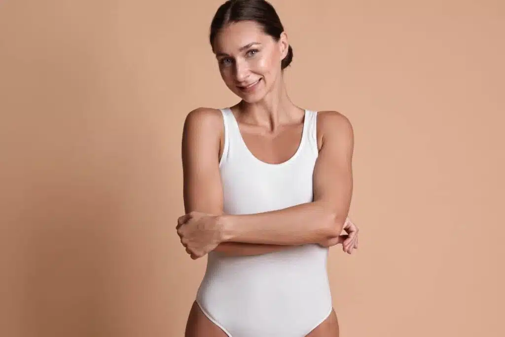 Woman with toned midsection wearing white bodysuit, representing tummy tuck preparation.