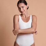 Woman with toned midsection wearing white bodysuit, representing tummy tuck preparation.