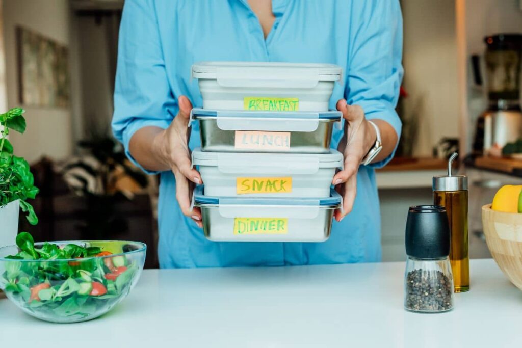 Person holding labeled meal containers for breakfast, lunch, snack, and dinner to support tummy tuck recovery.