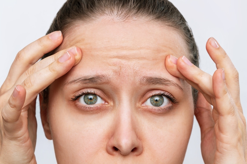 Close-up of woman lifting her eyebrows with fingers, showing typical signs treated by brow lift surgery.
