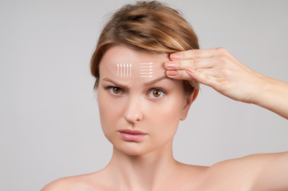 Woman pointing to forehead with diagram lines, illustrating brow lift concept and upper facial rejuvenation options.